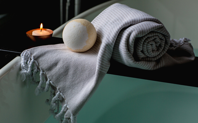 Towel on edge of bath with bathbomb and candle